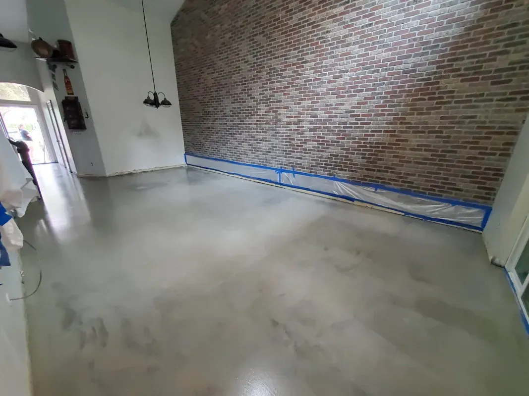 Empty room with polished concrete floor, brick wall, and blue painter’s tape along the baseboard.