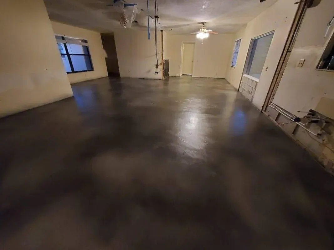 Empty indoor room with polished concrete floor, white walls, windows, and a ceiling fan.