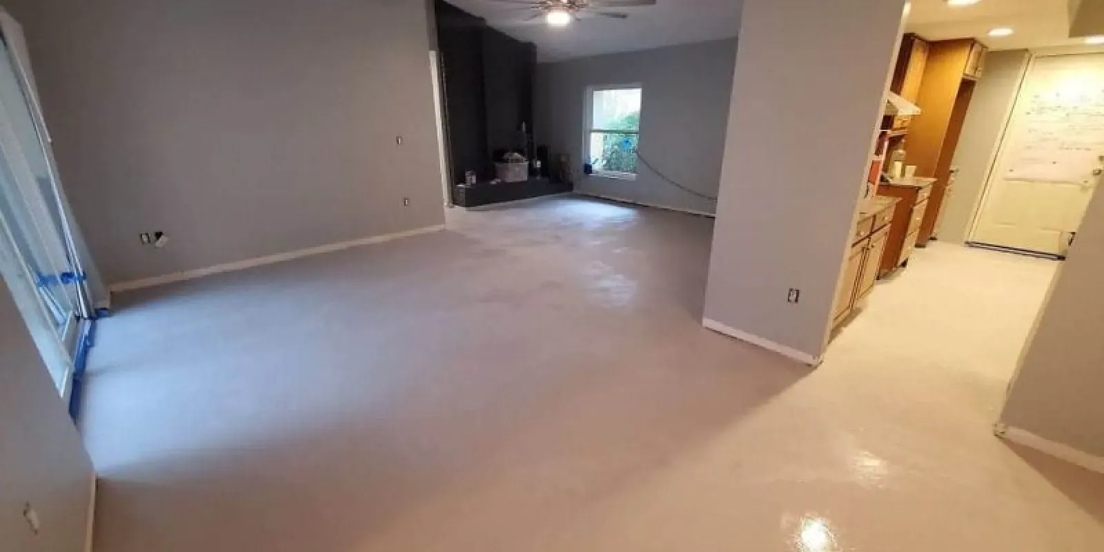 Empty beige living room with carpet, opening to a hallway and kitchen area in the background