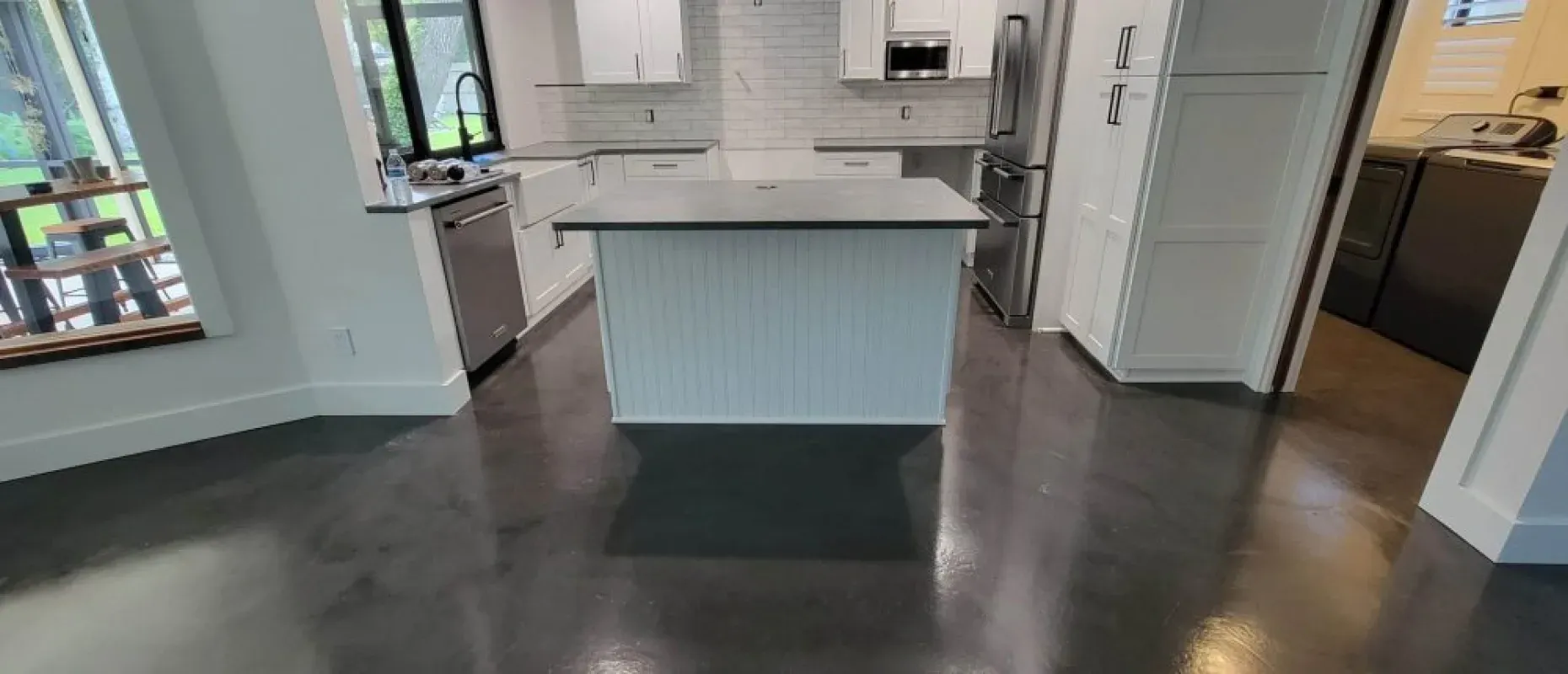 Bright kitchen with white island, dark floors, and large windows.