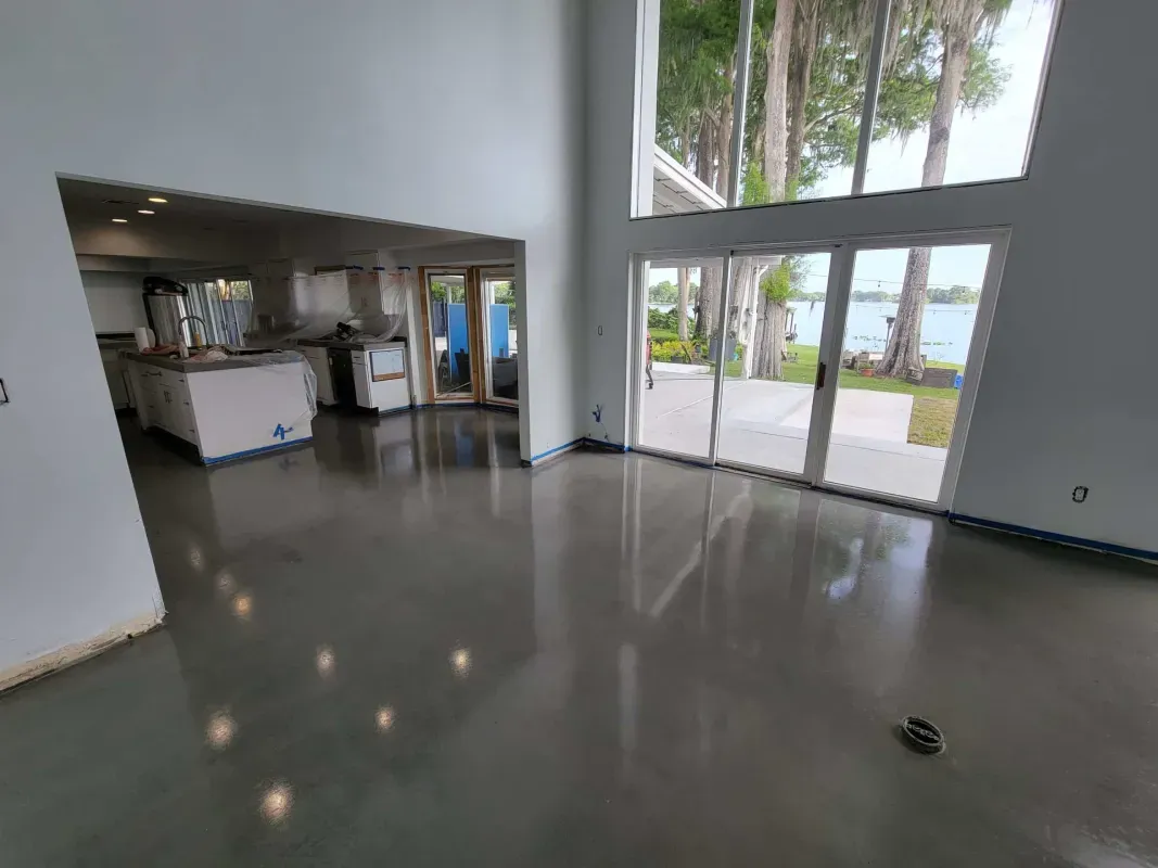 Empty modern room with polished concrete floor, large windows, and a kitchenette area.