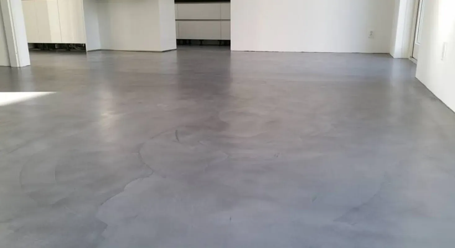 Empty concrete-floored room with white walls and doorway in the background