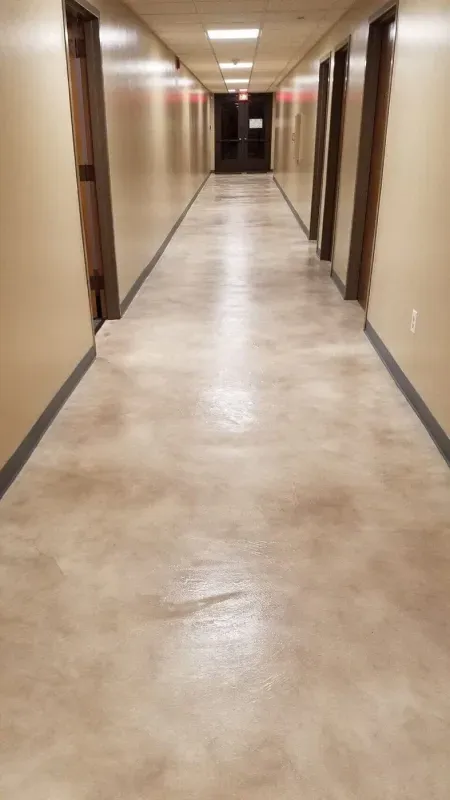 Empty beige hallway with closed doors and polished concrete floor under ceiling lights