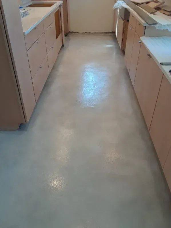 Narrow kitchen aisle with beige cabinets and a light gray floor under bright overhead light