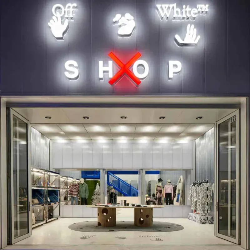 Bright fashion boutique storefront with white interior and clothing racks behind open glass doors