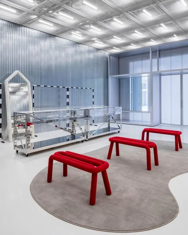 Modern industrial room with red stools, a circular gray rug, and metal machinery under bright lighting