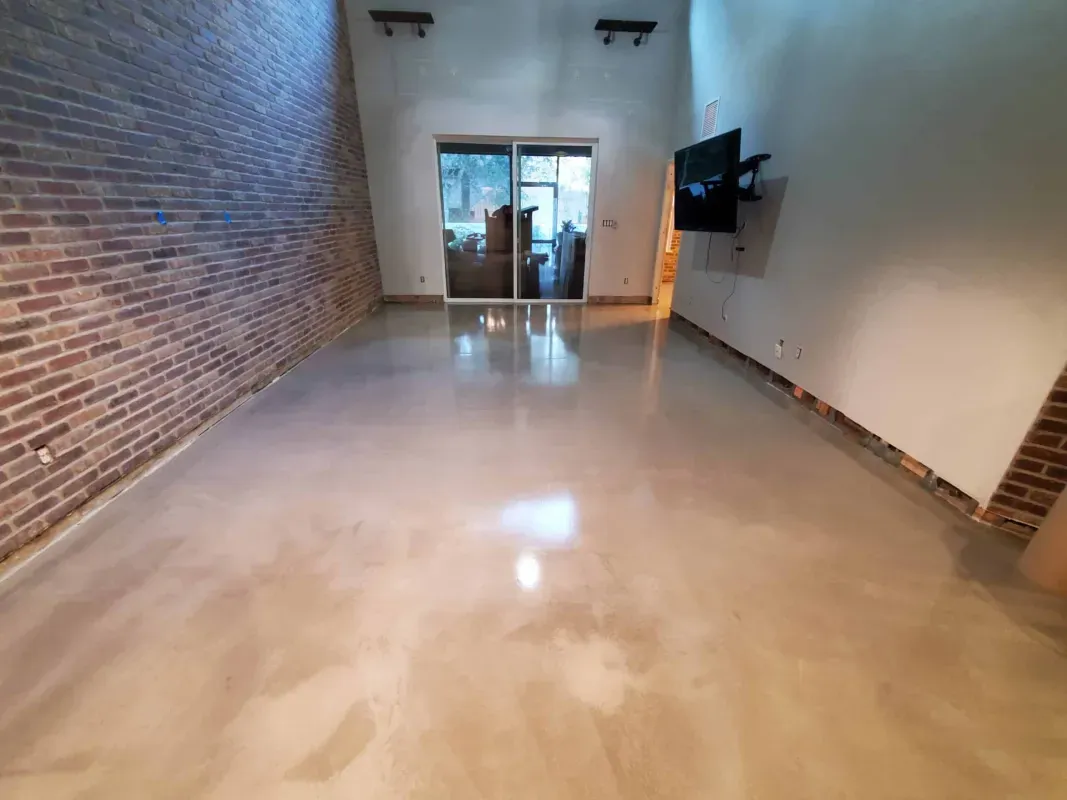 Empty modern room with polished concrete floor, exposed brick wall, and glass doors at the far end