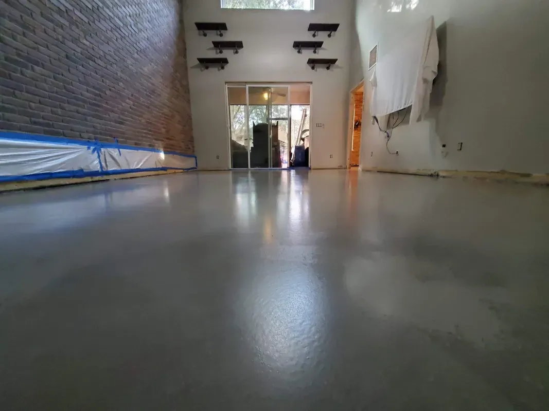 Empty long hallway with glossy floor, brick wall on left, white walls on right, and an open doorway ahead