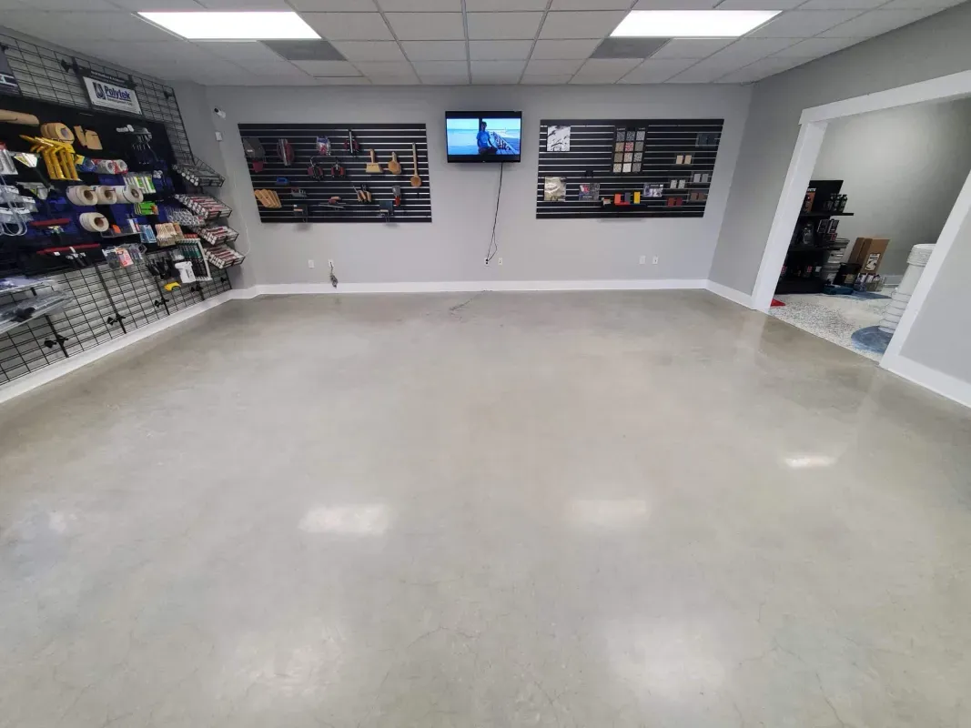 Empty retail showroom with gray floor, wall-mounted shelves, and a TV on the back wall.