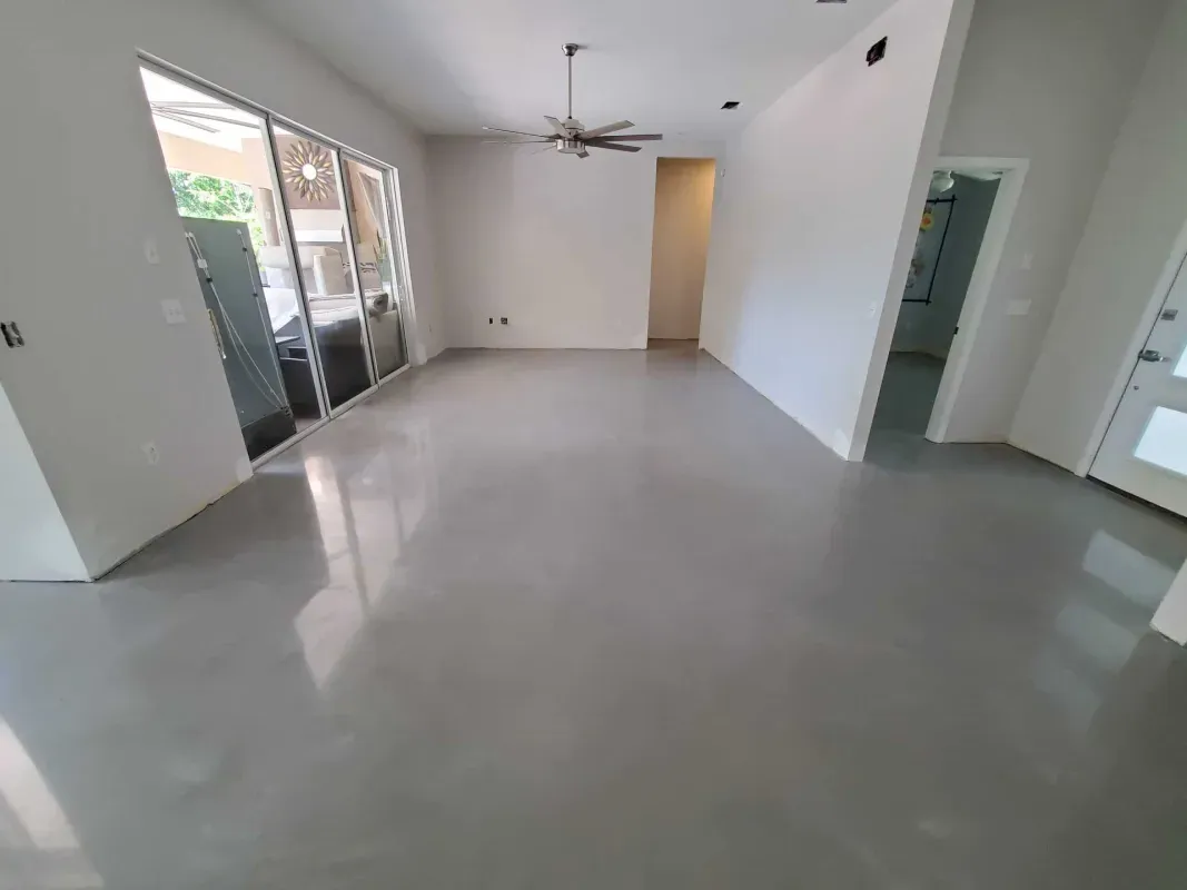 Empty modern living room with glossy gray floor, white walls, ceiling fan, and sliding glass doors.
