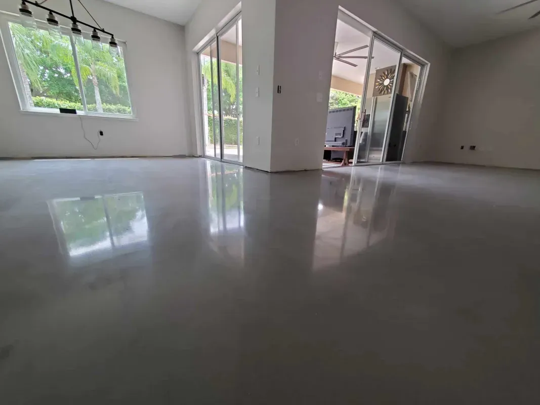 Empty modern room with glossy floors, large windows, and sliding glass doors opening to a patio garden.