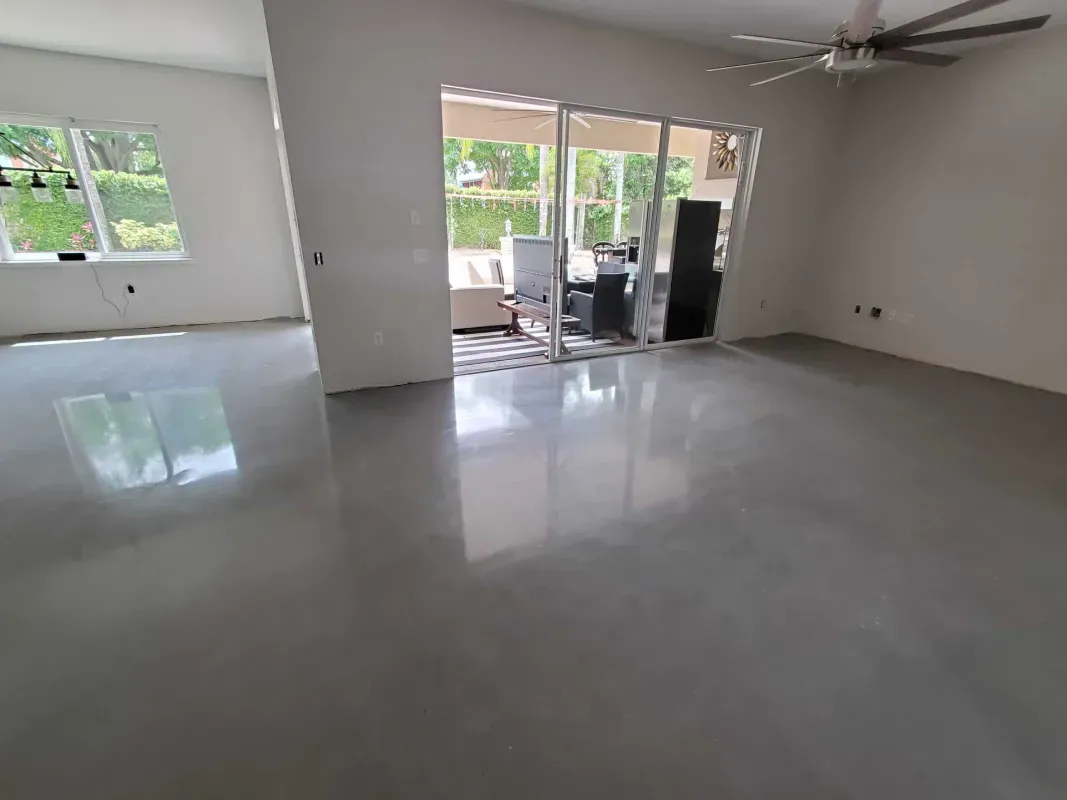 Empty living room with glossy gray floor, white walls, large windows, and sliding glass doors to a patio.