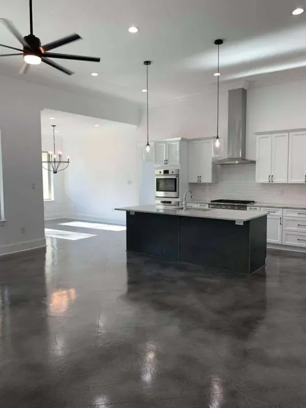 Modern open-concept kitchen and living area with white cabinets, black island, and polished concrete floor