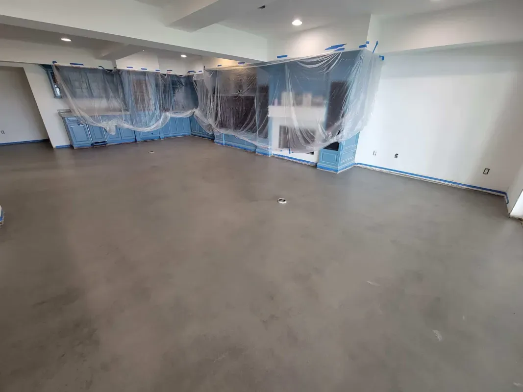 Empty room with gray floor and blue plastic sheeting covering walls and windows during renovation