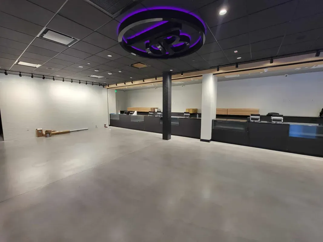 Empty modern showroom with concrete floor, white walls, black counters, and a purple-lit ceiling fixture.
