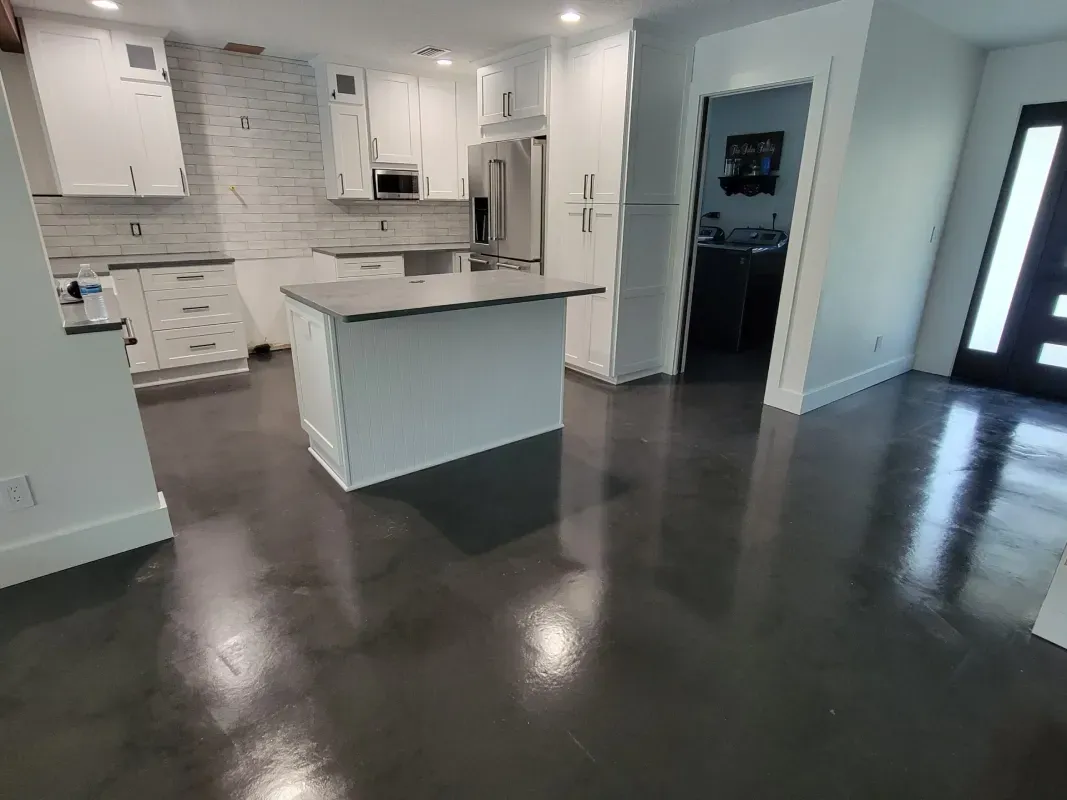 Modern white kitchen with island, dark hardwood floors, stainless appliances, and open entryway
