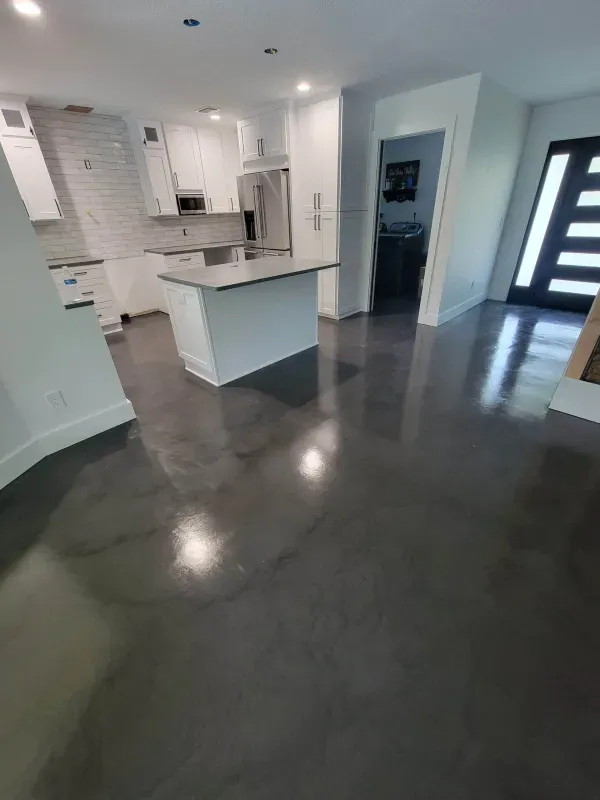Open-concept modern kitchen with white cabinets, island, and dark polished concrete floor