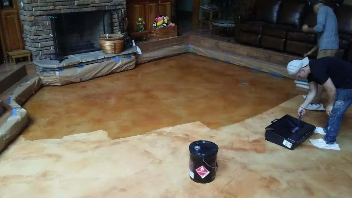 Person cleaning a large tan floor by hand with a black bucket in a rustic stone room