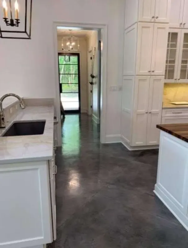 Bright white kitchen with island, sink, and dark concrete floor leading to a doorway and garden view