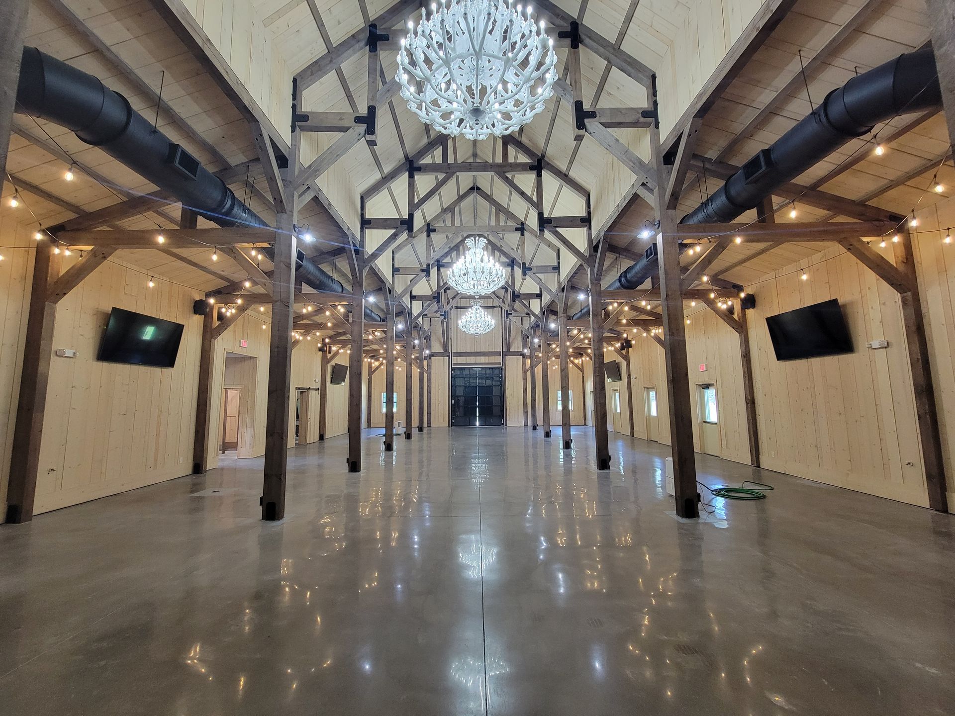 Spacious industrial hall with exposed beams, hanging lights, and a polished reflective floor