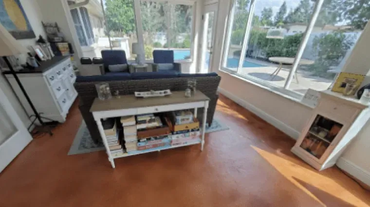 Bright sunroom with sofa, coffee table, large windows, and orange floor.