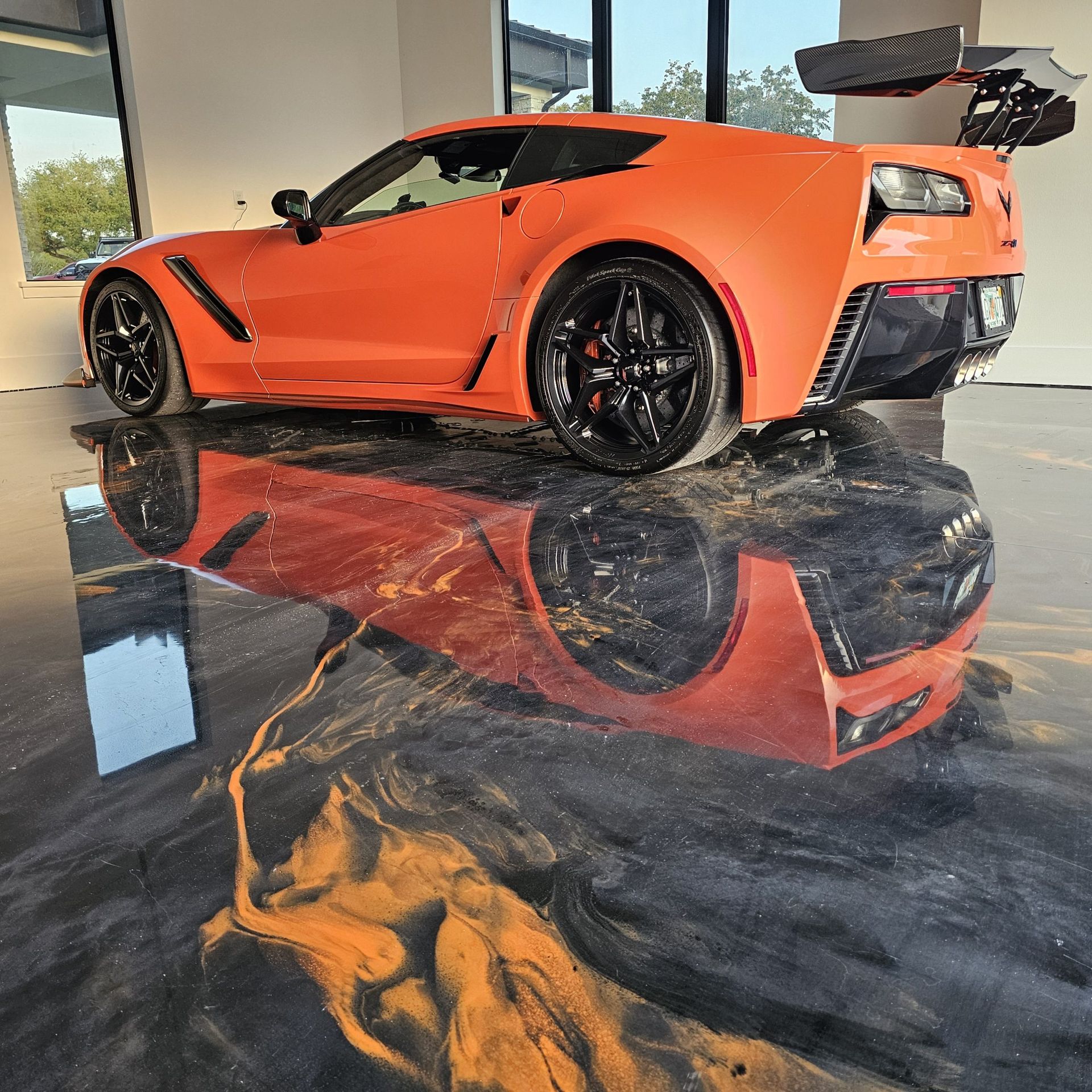 Orange sports car displayed indoors on a glossy black floor reflecting its image.