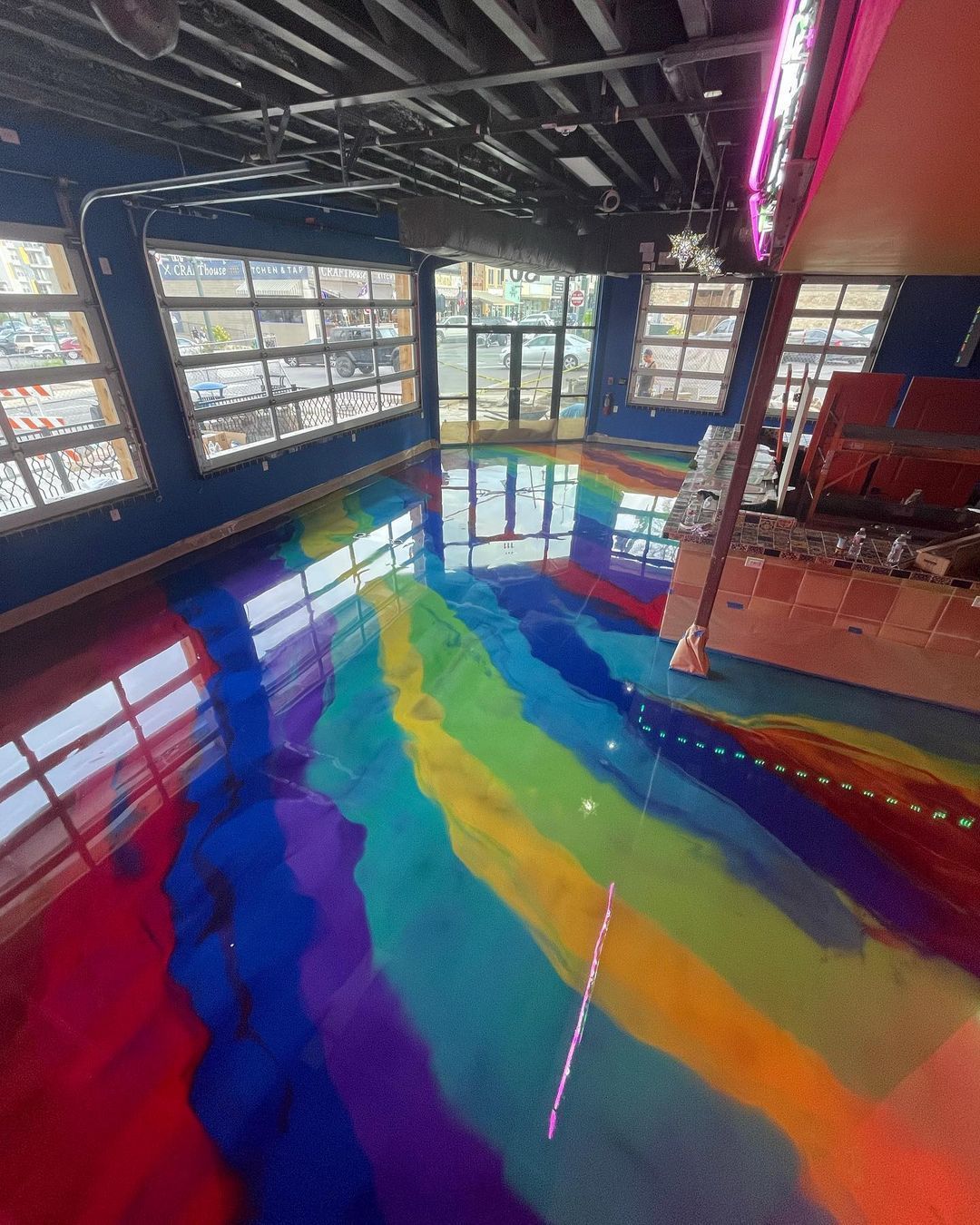 Colorful rainbow floor mural in a bright indoor room with large windows and neon lighting