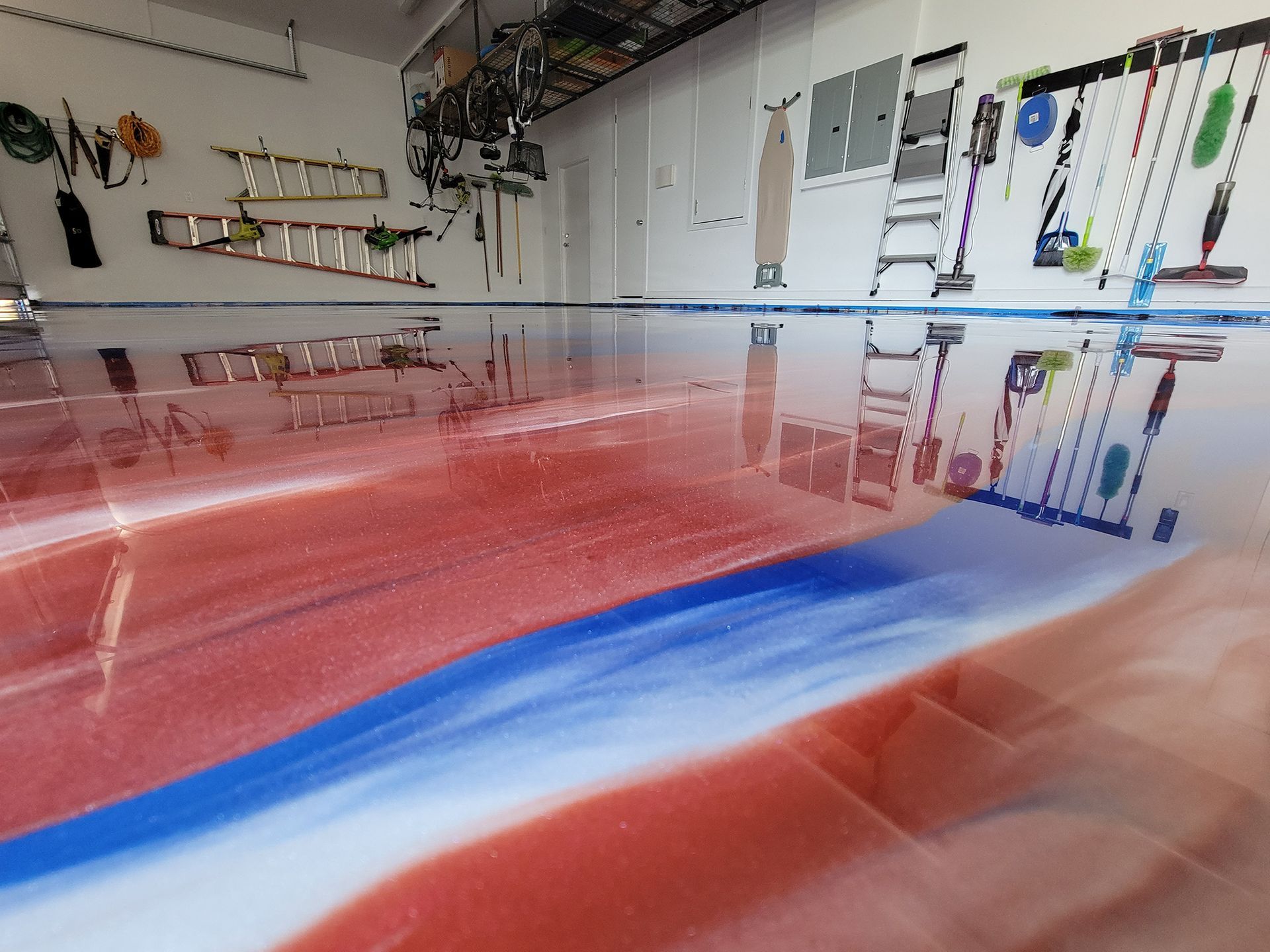 Long red workbench with blue stripe in a workshop or garage, shelves and tools along the back wall