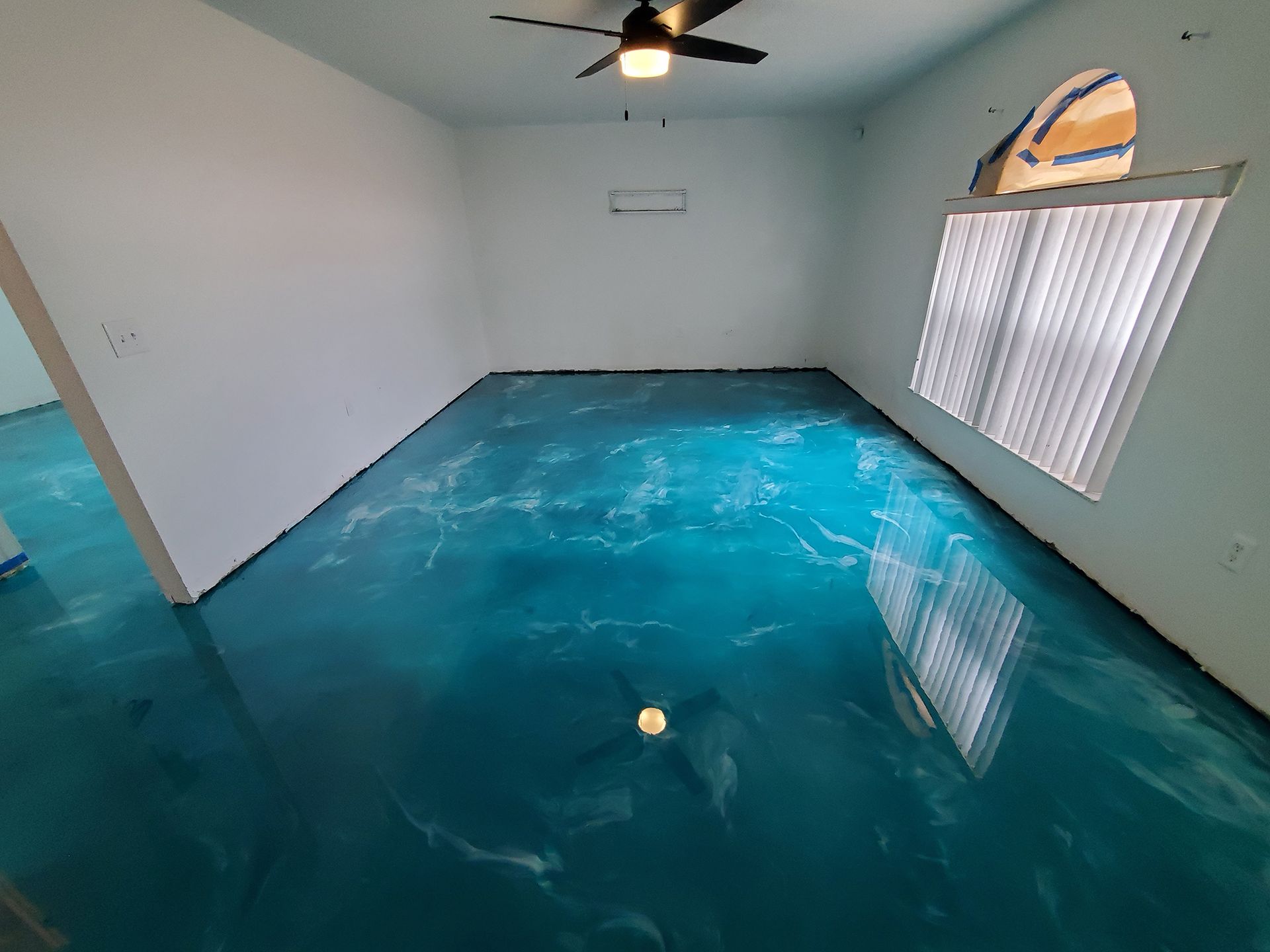 Empty room with glossy blue floor, white walls, ceiling fan, and window blinds.