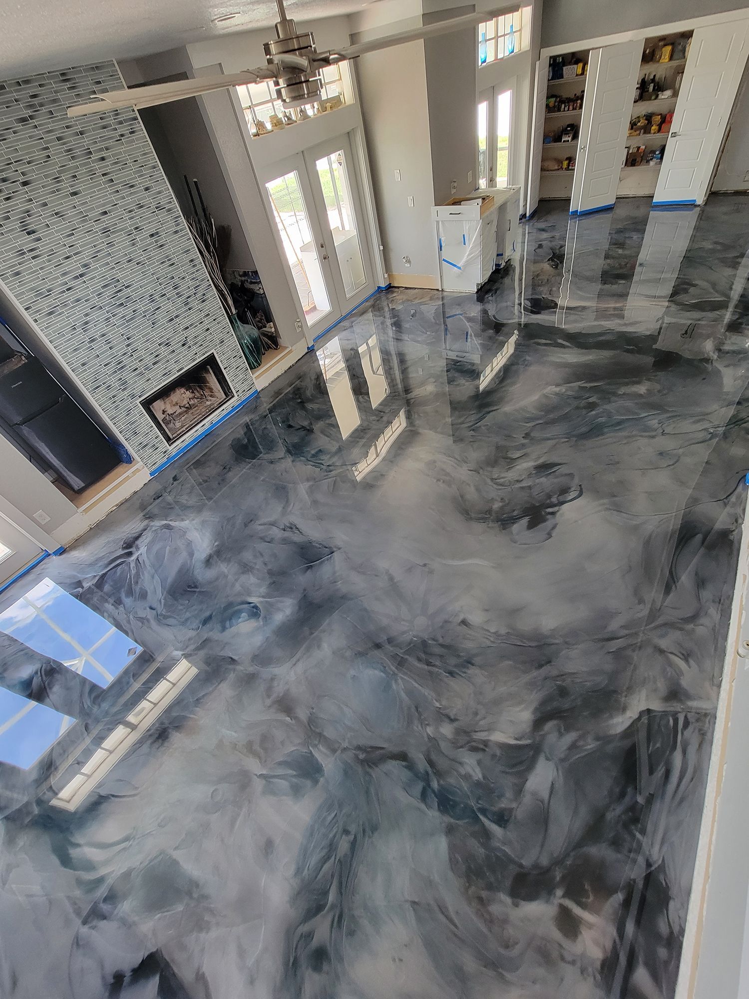 Polished gray epoxy floor in a bright modern room with large windows and a tiled fireplace wall.