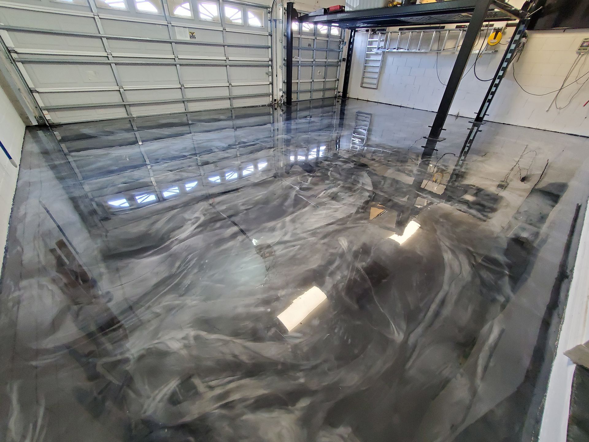 Shiny epoxy floor in an empty garage with a large open door and reflective ceiling lights