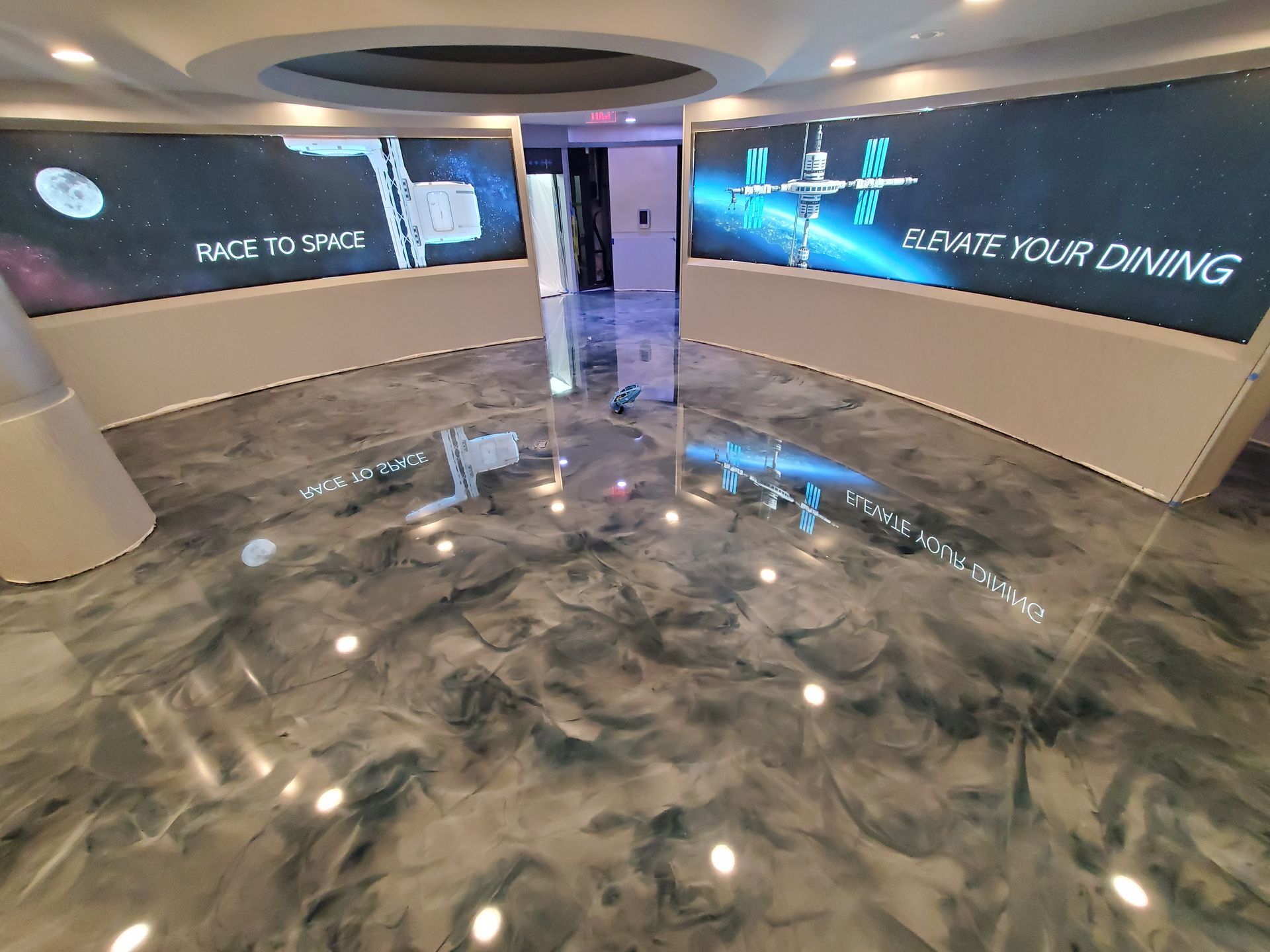 Futuristic lobby with glossy floor, curved walls, and blue-lit display screens reading
