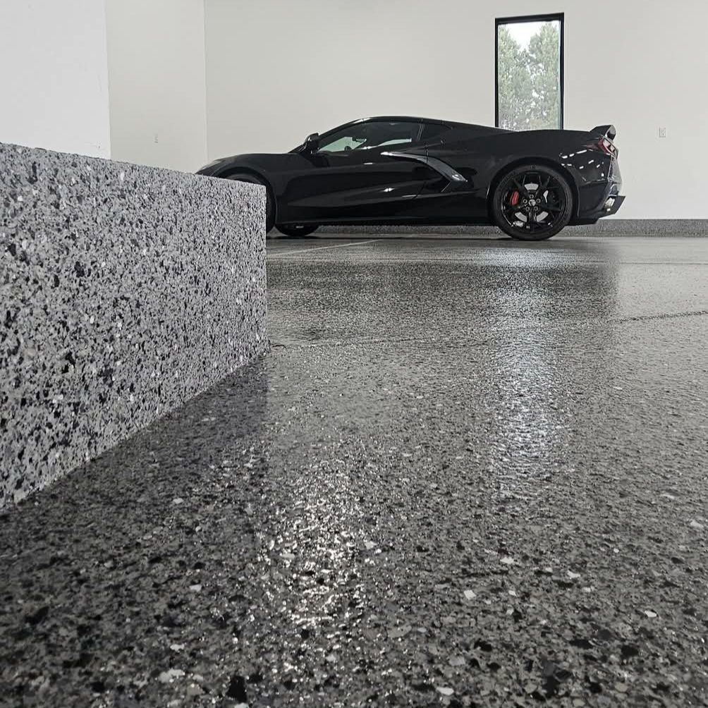 Black sports car parked in a minimalist garage with speckled concrete floor