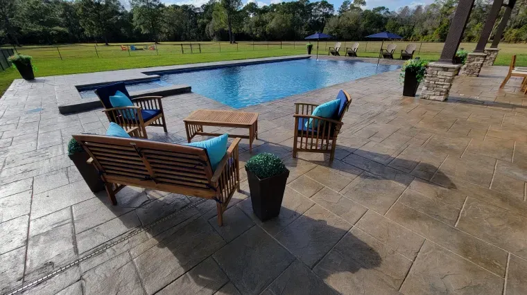 Outdoor patio with lounge chairs, a pool, and a grassy backyard under a clear sky