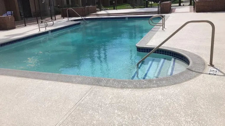 Outdoor swimming pool with clear blue water, curved edge, and metal handrail on a sunny day