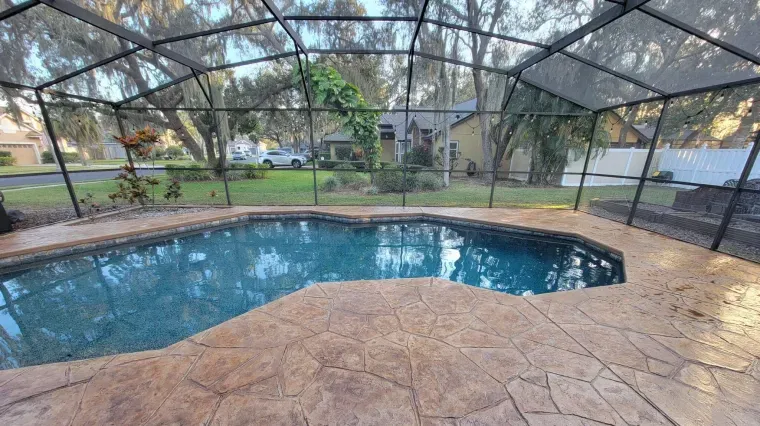 Screened-in backyard pool with blue water and tan stone deck at dusk