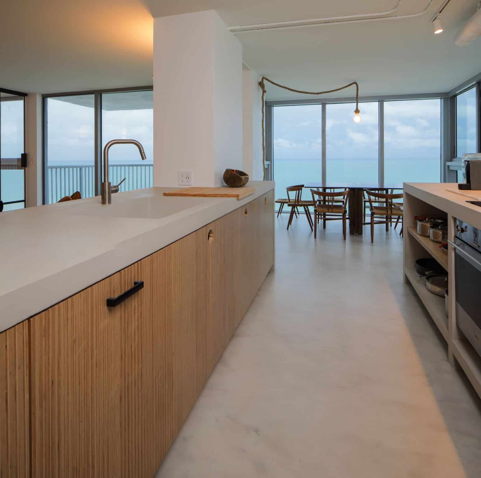 Modern kitchen opening to a bright ocean-view dining area with floor-to-ceiling windows