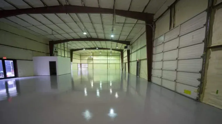 Empty industrial warehouse interior with glossy floor, metal walls, and overhead beams