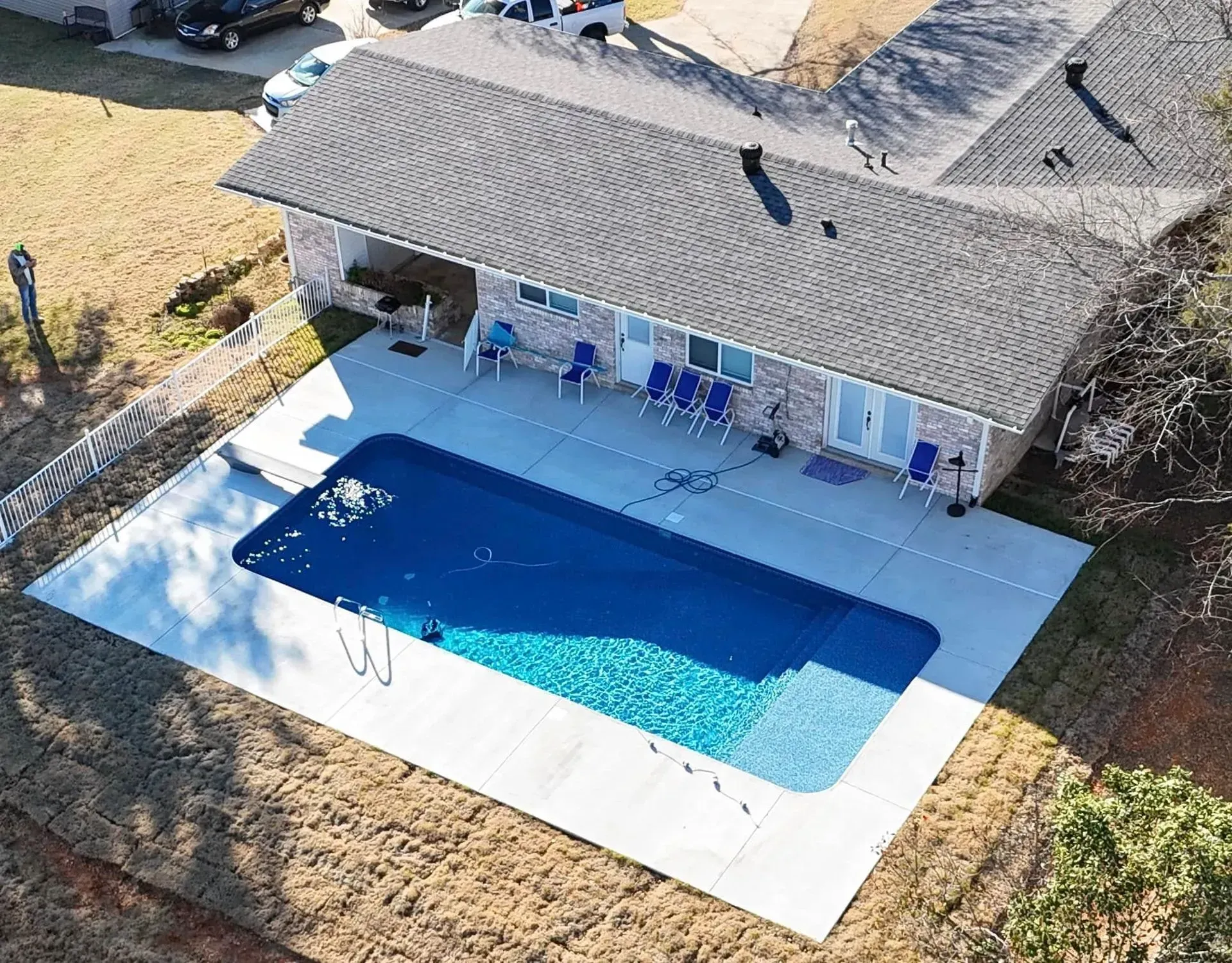 Aerial view of a house with a rectangular swimming pool covered in blue. Several blue chairs sit near a wall.