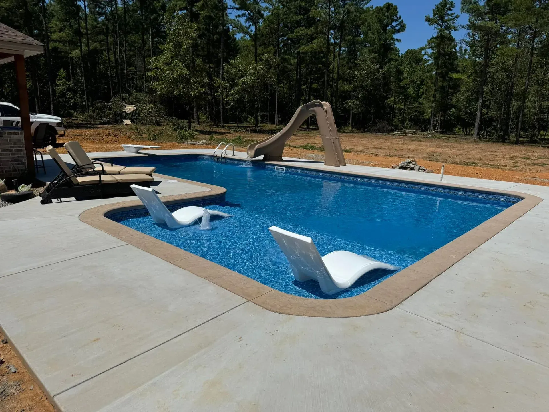 Rectangular swimming pool with slide, lounge chairs, and concrete patio.