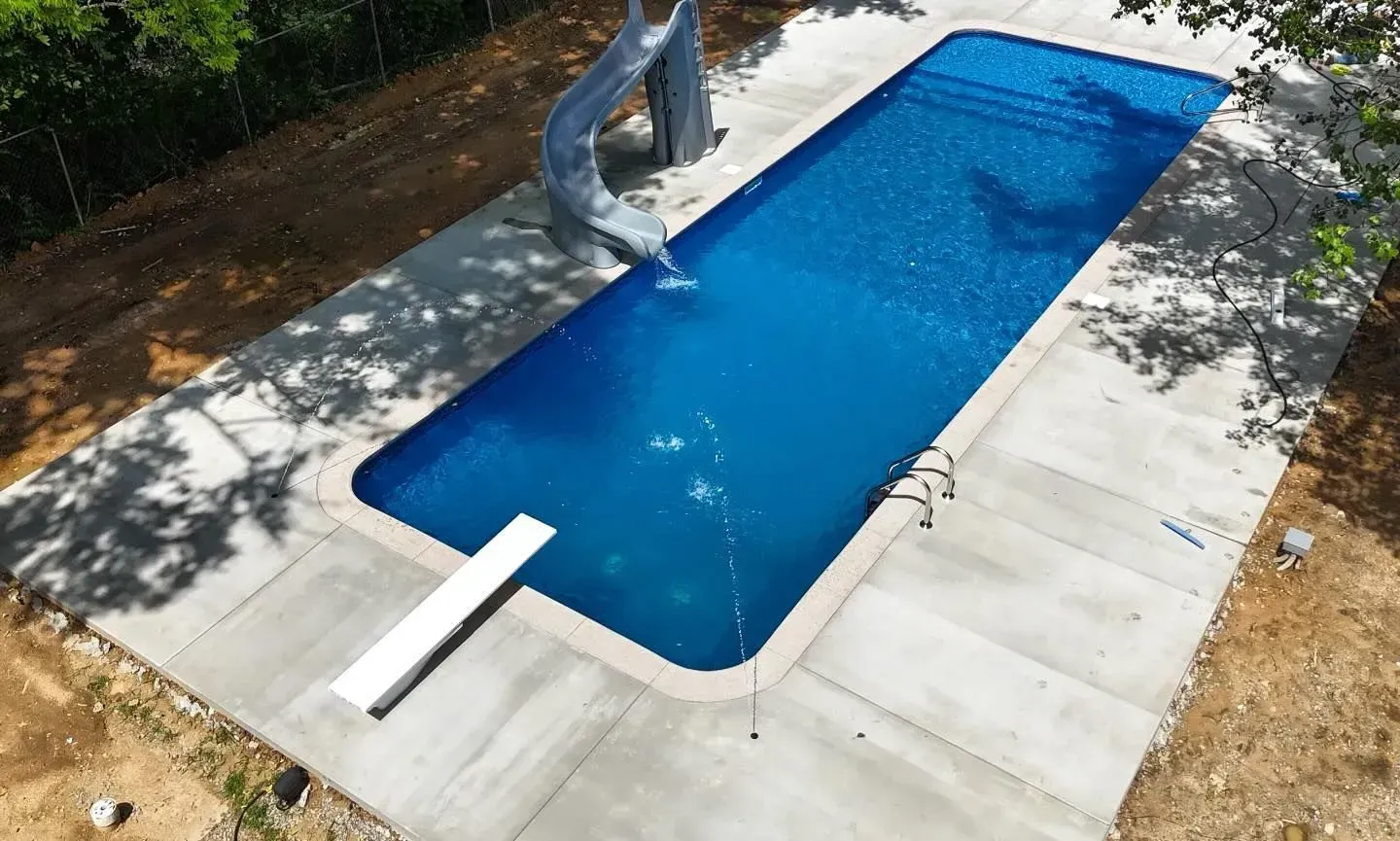 Aerial view of a rectangular pool with a slide and diving board, surrounded by concrete.
