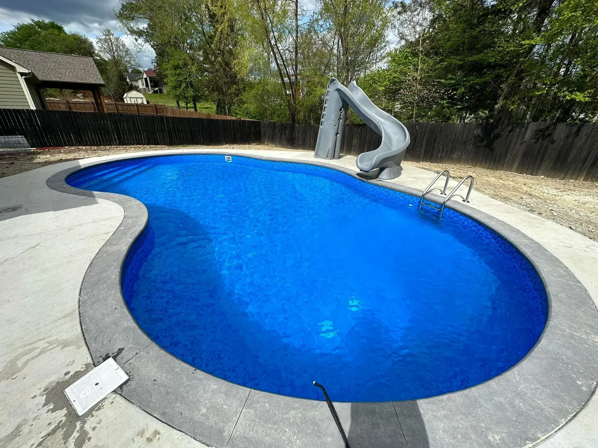 Swimming pool with a blue interior, concrete surround, and a gray slide.