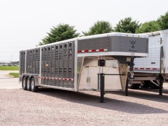 Livestock trailer parked on a gravel lot; gray, with slotted sides.