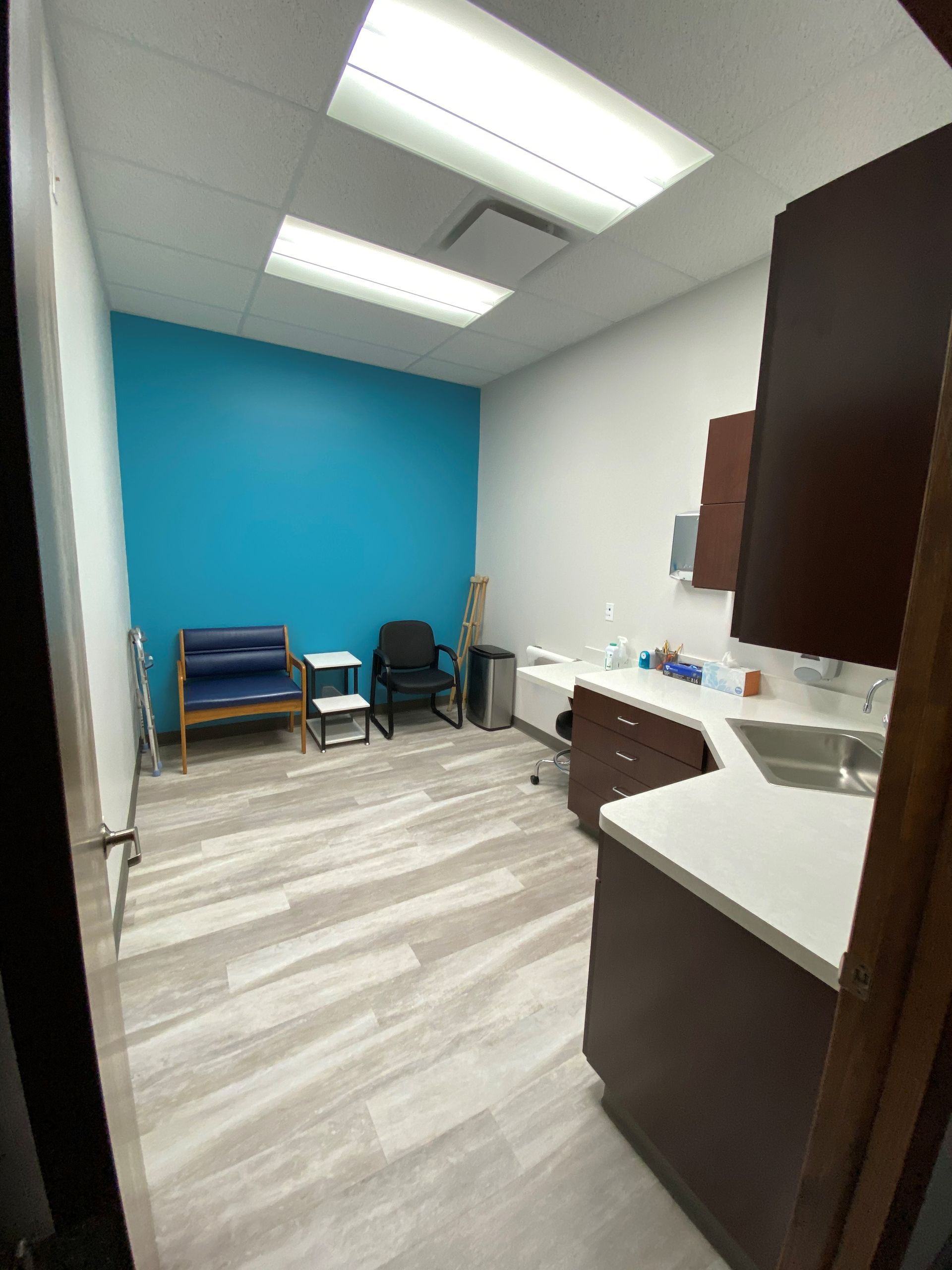 A room with a blue wall , a couch , chairs , and a sink.