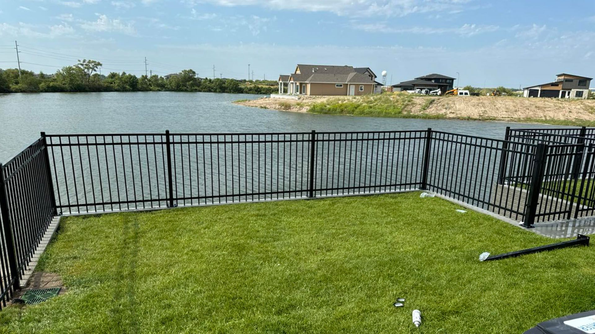 A fence surrounds a lush green lawn with a lake in the background.