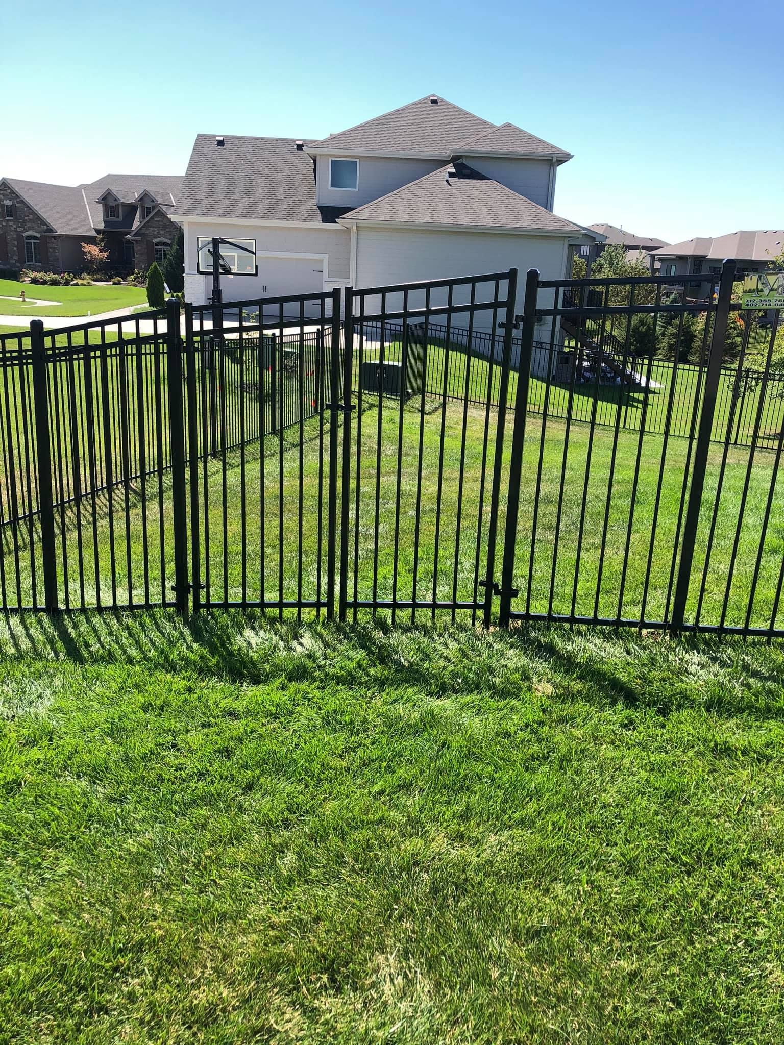 A black fence surrounds a lush green yard in front of a house.