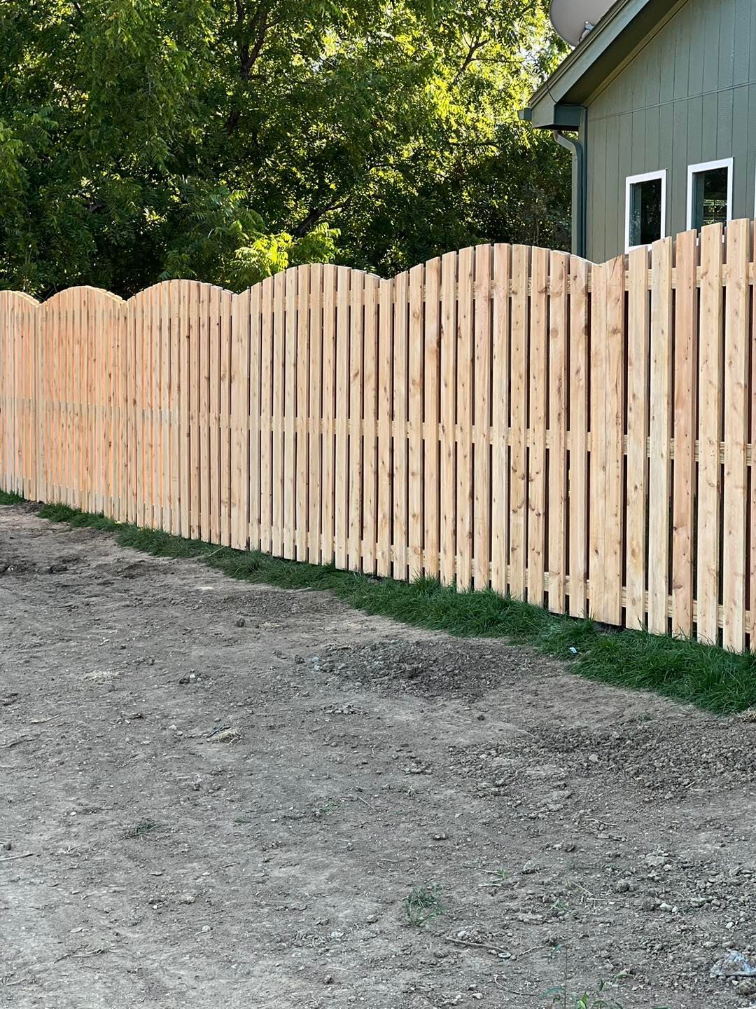 A wooden fence is sitting on the side of a dirt road next to a house.