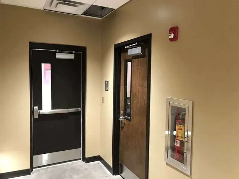 Interior hallway with black and wood doors, beige walls, and a fire extinguisher cabinet.
