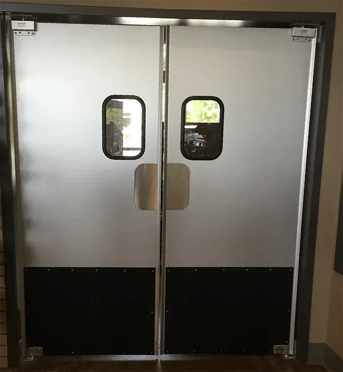 Closed silver double doors with small windows and black lower panels in a hallway