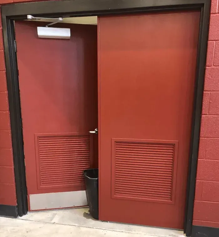 Partially open red double doors with louvered vents in a red-walled hallway